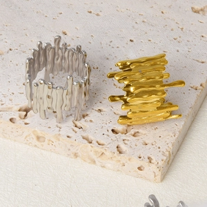 Detail of irregular liquid metal rings in gold and silver finish on beige stone
