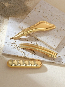 Detailed view of three unique gold metal hair clips on a natural stone and sand surface