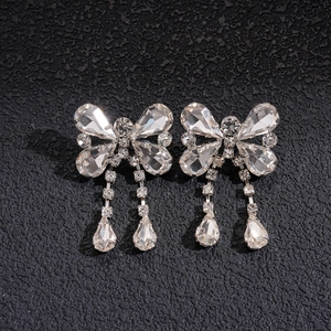 Macro shot of sparkling silver bow earrings with crystal water drop tassels on black texture