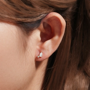 Close-up of golden cartilage earrings with heart chain and pear-cut clear gemstones