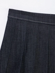 Detailed macro view of dark blue denim pleated skirt with white contrast stitching accents