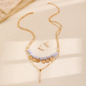 Dettaglio della collana a strati bohémien dorata e orecchini con perline viola su sabbia