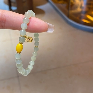 Détail du bracelet en perles vert clair avec pendentif Fu doré et perle d'ambre