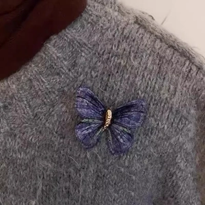 Elegant butterfly embroidery brooch with gold accent pinned on a grey knitted sweater