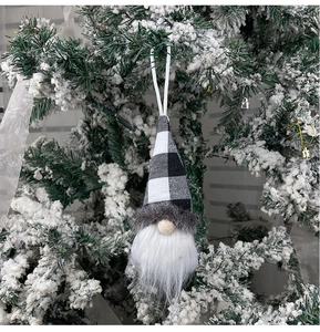 Christmas gnome ornament with black and white plaid hat hanging on a snowy Christmas tree