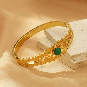 Detail of gold hollow-out bangle with a green gemstone on a white stone base