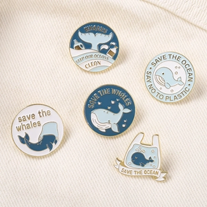 Set of 5 enamel whale pins with 'Save the Ocean' slogans on beige fabric texture