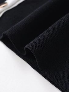 Close-up of black ribbed knit cardigan cuff with white trim and gold button detail