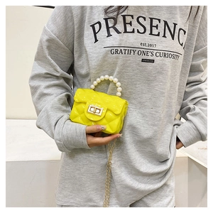 Detail of yellow quilted jelly handbag with pearl handle and golden chain strap on model