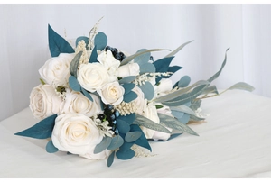 Detailed side view of a white rose cascade bridal bouquet with deep blue foliage accents
