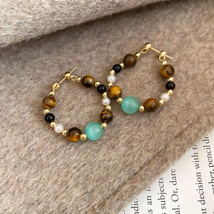 Detailed view of beaded hoop earrings with tiger eye and pearls on soft beige fabric