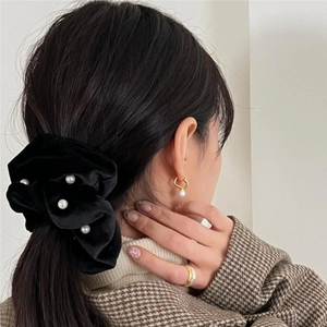 Detail of elegant black velvet hair scrunchie with pearls worn by a model in soft light