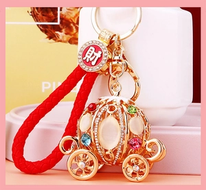Detail of golden pumpkin carriage keychain with colorful rhinestones and red woven cord