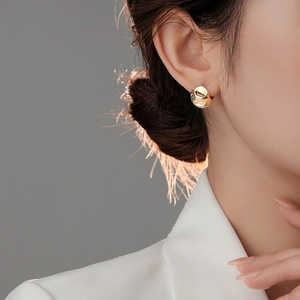 Close-up of model wearing gold irregular hammered metal hoop earrings in a minimalist style