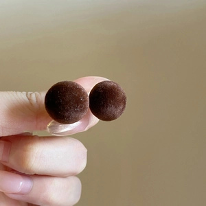 Close-up of dark brown flocked round stud earrings with a soft matte velvet texture