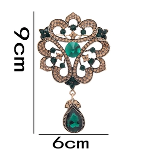 Detail view of vintage hollow brooch with emerald green stones and 9cm length dimensions