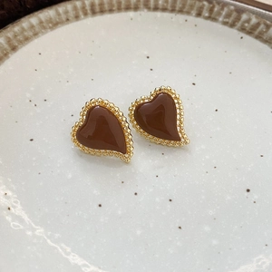 Detailed close-up of heart-shaped gold-rimmed earrings in a beige ceramic dish