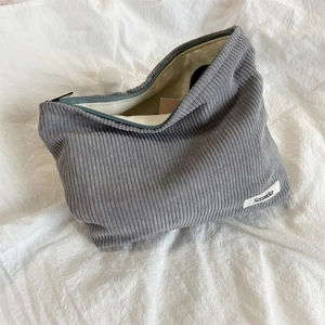 Detailed view of gray corduroy makeup bag with zipper on soft white fabric background