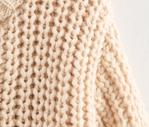 Close-up of beige chunky knit cardigan showing soft wool texture and detailed stitch patterns