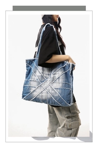 Detail of blue denim tote bag with raw edges and distressed patchwork design on model