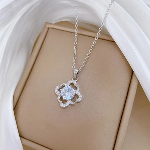 Close-up of sparkling hollow four-leaf clover pendant with zircon on white silk fabric