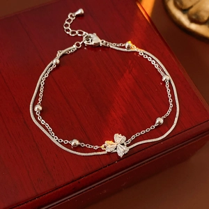 Detail eines silbernen Doppelarmbandes mit Kleeblatt-Zirkonia-Anhängern auf Holzoberfläche