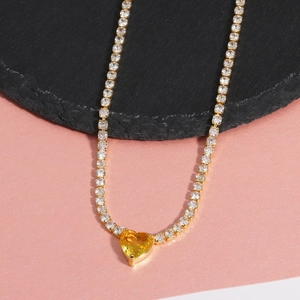 Detailed close-up of a gold necklace featuring a heart-shaped yellow gemstone and zircons