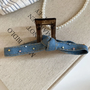 Close-up of denim bow hair claw clip with colorful rhinestones on a textured background