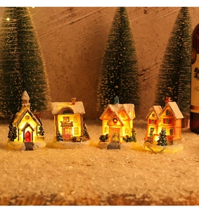 Detail view of four miniature Christmas houses with glowing lights on faux snow background