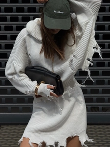 Robe en maille blanche à effet usé avec casquette olive devant une porte industrielle