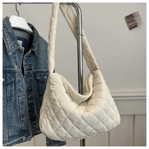 Detail of a large quilted corduroy tote bag in cream white hanging by a denim jacket