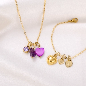 Close-up of gold paperclip chain jewelry set with purple gemstones and heart pendants