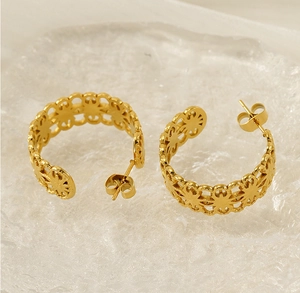 Close-up of gold plated C-shaped earrings featuring hollow sunburst floral patterns