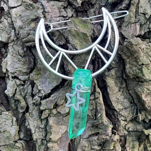 Detail of silver moon hair clip with green crystal and star charm on bark