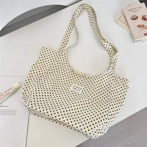 Close-up of a white canvas tote bag featuring black polka dots and a small brand label
