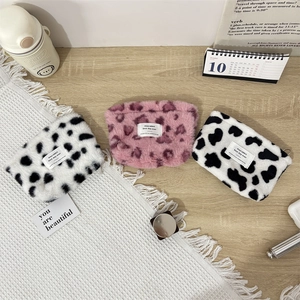 Plush makeup bags in cow and leopard patterns on a warm minimalist lifestyle background