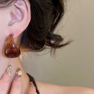 Close-up of a model wearing large C-shaped resin earrings with amber tortoise shell texture