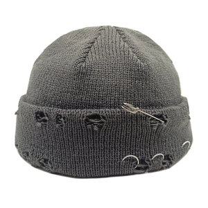 Detail of dark grey knit beanie featuring distressed holes, silver rings and a safety pin
