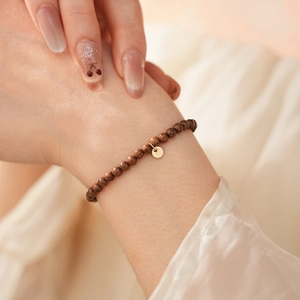 Close-up of minimalist agarwood bead bracelet with a round golden metal charm on wrist
