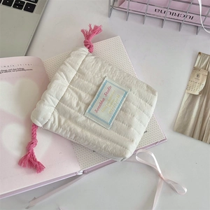 Detailed view of a white quilted drawstring pouch with pink cords and brand label