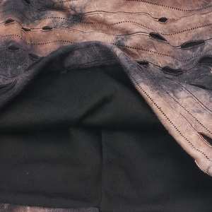 Macro shot of tie-dye knit fabric with distressed hole details and warm black lining