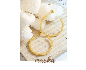 Detail shot of gold-plated bamboo texture C-shaped hoop earrings on a stone pedestal