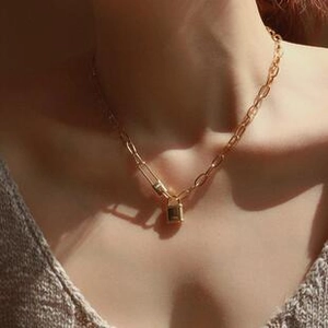 Close-up of golden paperclip chain necklace with a polished padlock pendant on neck