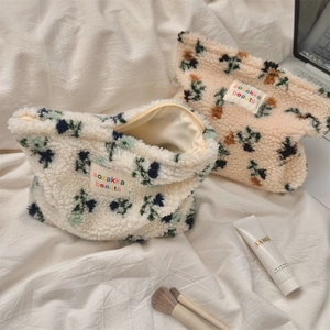Detail of floral plush makeup bag showing soft texture and colorful embroidered label