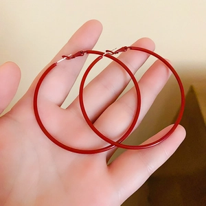 Detail showing hand holding large Ancora red enamel hoop earrings with silver needles