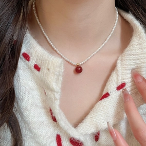 Close-up of pearl necklace featuring a deep red round pendant on a knit sweater background