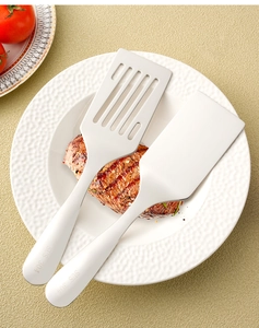 Macro view of 304 stainless steel spatula set and slotted turner with steak on a white plate