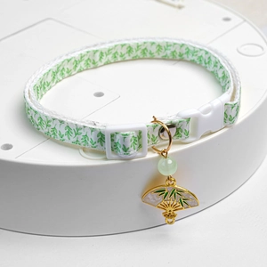 Detail of pet collar with bamboo leaf pattern and golden fan charm on a white stand