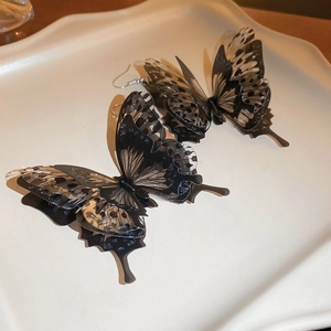 Detail of dark acrylic butterfly earrings with realistic spotted wings on white tray