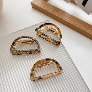 Three medium-sized semi-circular hair claws with amber and marble textures on a glass tray